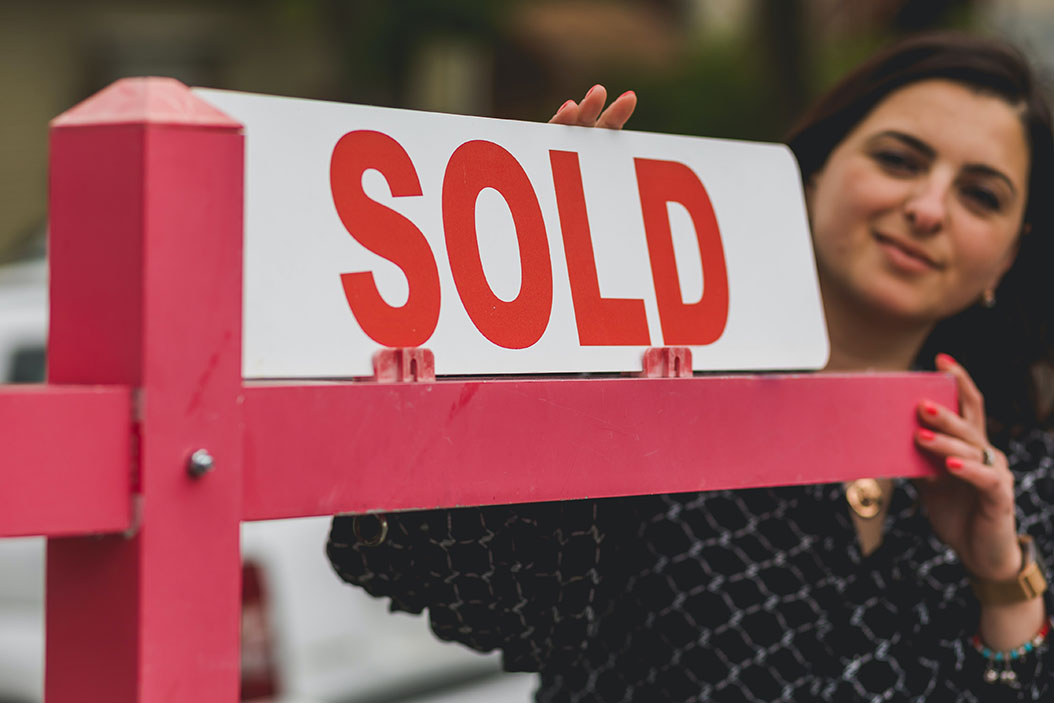 women standing behind 'sold' lawn sign