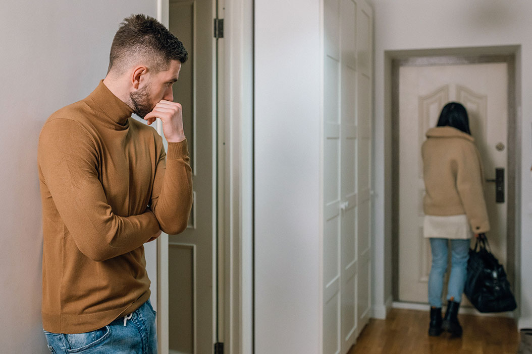 Couple fighting, woman walking out of an apartment while sad man looks on